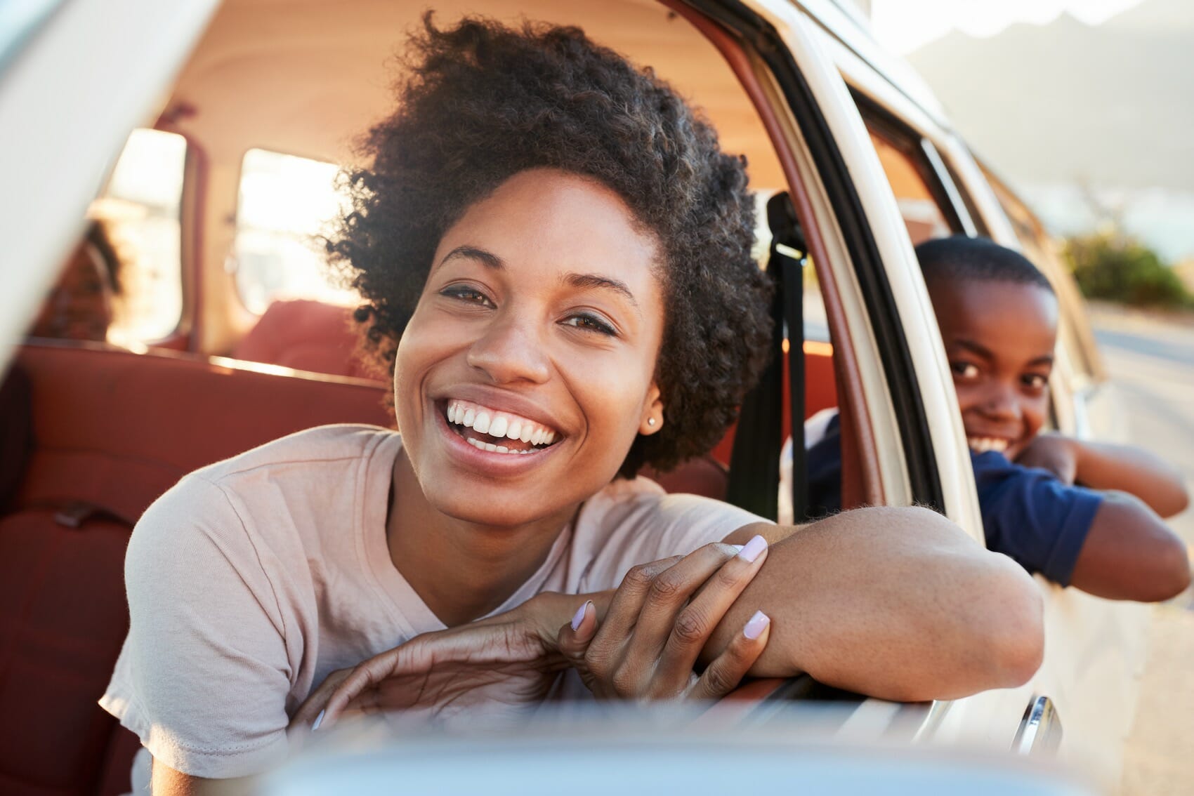 Mother and son on road trip with heads peering through open windows in their parked car